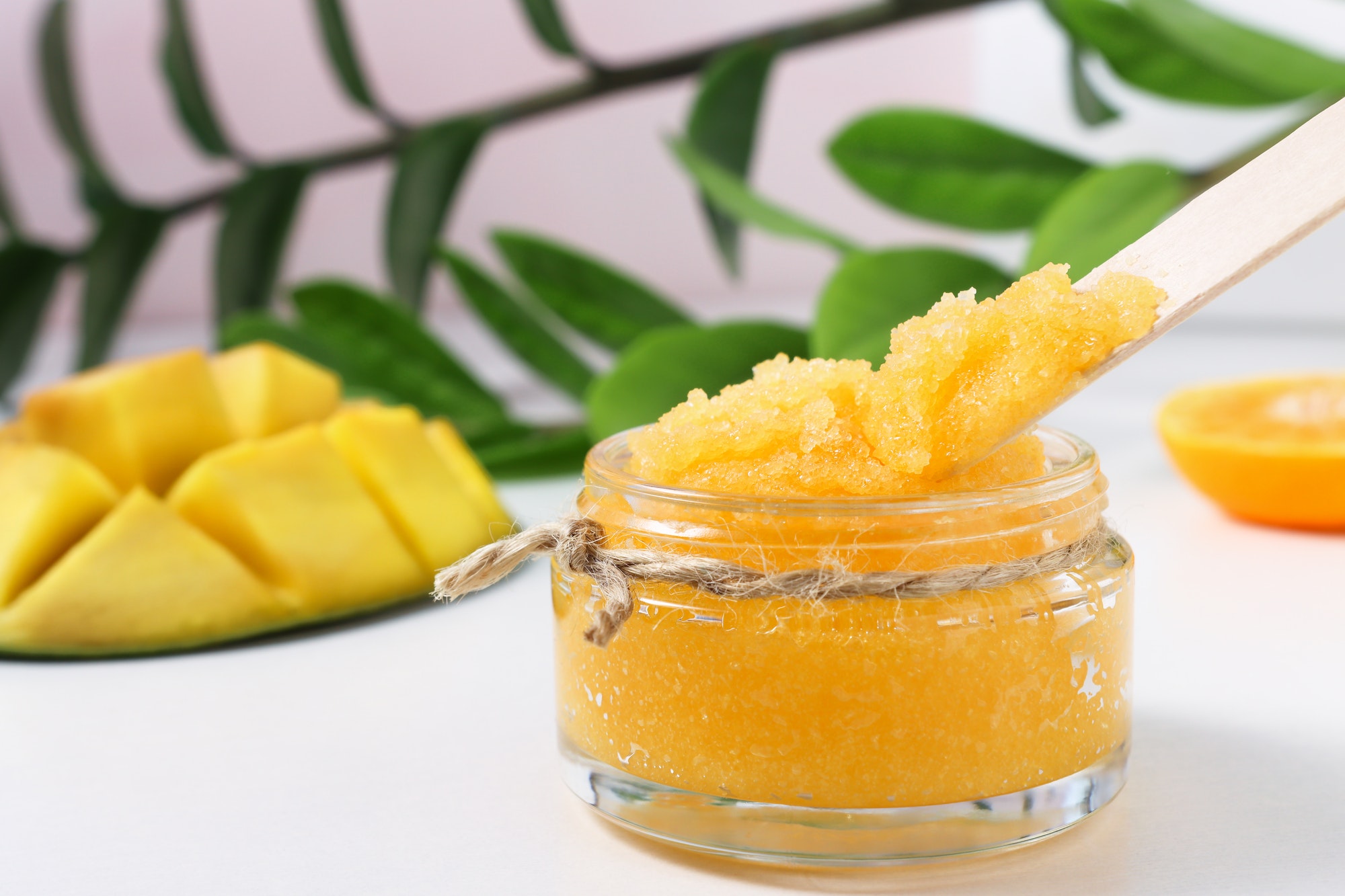 Homemade cosmetic product with mango and green leaves of the plant on the background.